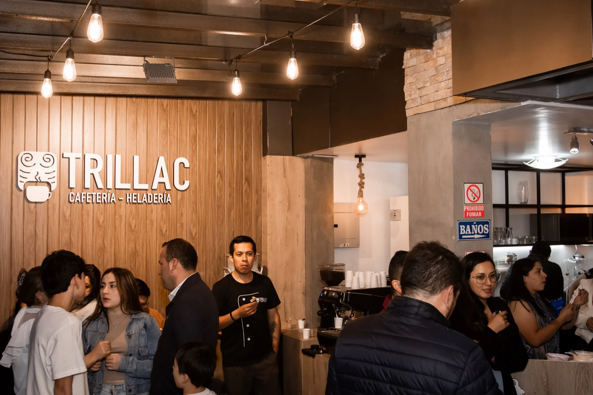 Barra de espresso de Trillac con el muro de madera y el letrero iluminado, llena de clientes