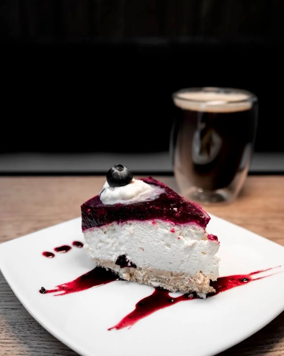 Porción de cheesecake con jalea de frutos rojos junto a una taza de café negro