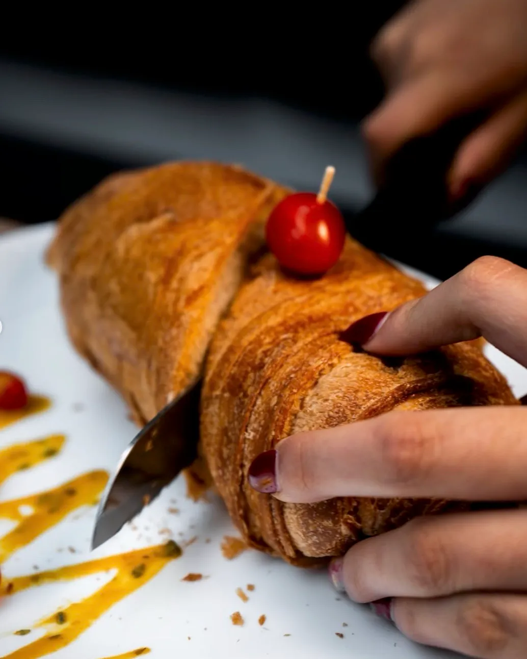Manos cortando un pan hojaldrado salado con tomate cherry y salsa de hierbas