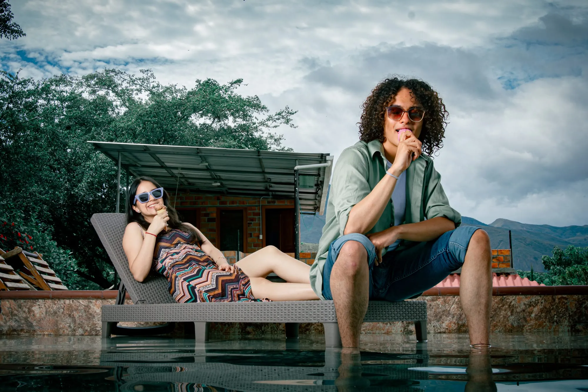 Pareja con conos de helado junto a la piscina, con montañas al fondo