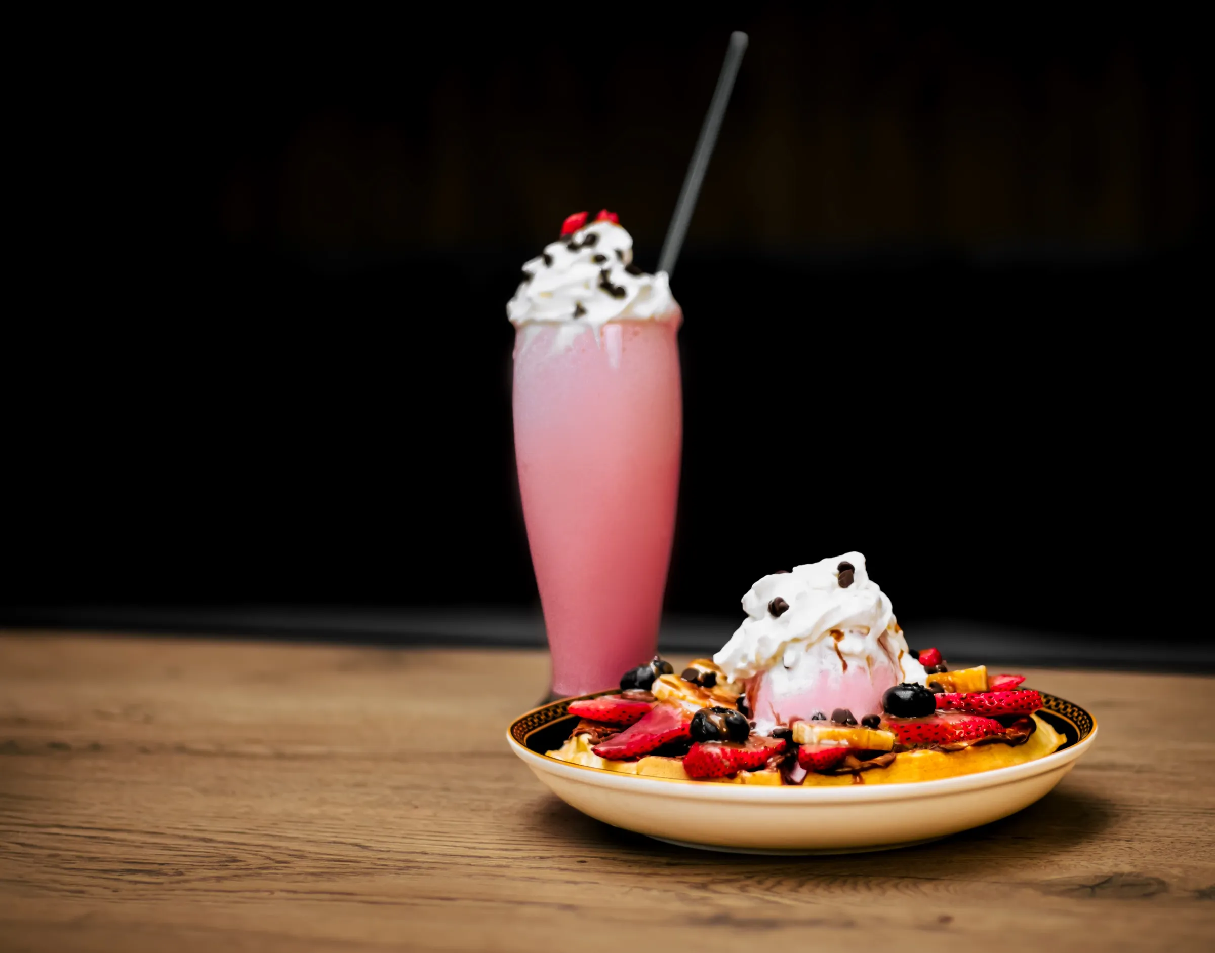 Malteada de fresa con crema y waffle con helado y frutos rojos sobre una mesa de madera