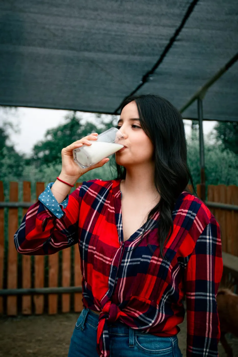 Mujer bebiendo un vaso de leche de cabra bajo la malla del establo